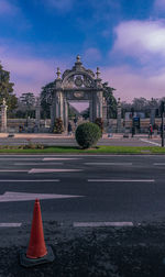 Road by building against cloudy sky