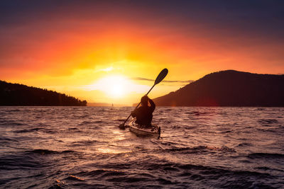 Silhouette man in sea against sky during sunset