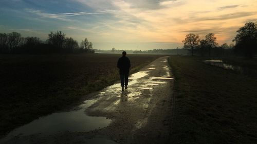 Rear view of silhouette man walking on road against sky