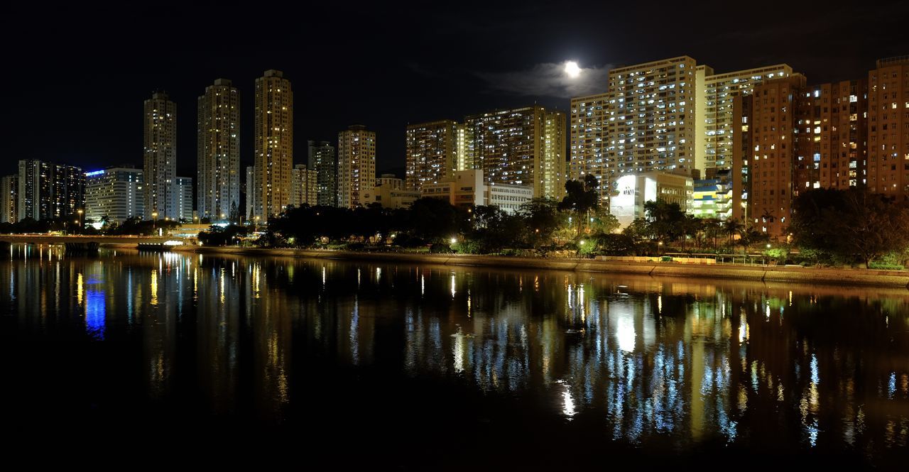 ILLUMINATED BUILDINGS BY LAKE AGAINST SKY IN CITY