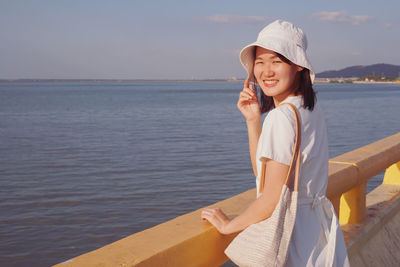 Portrait of beautiful woman standing by sea against sky