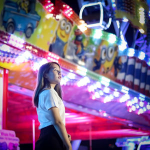 Low angle view of young woman looking away while standing in amusement park