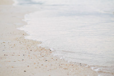 Closeup macro shot of sea ocean wave water with white foam, sandy beach background 