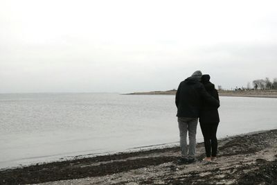 Rear view of man and woman walking at sea shore against sky