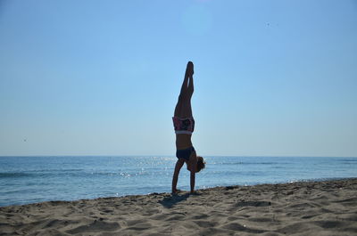 Woman doing handstand at shore of beach against sky