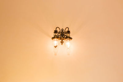 Close-up of illuminated lamp on table against orange background