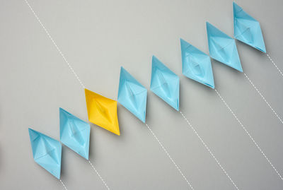 A row of paper boats on a gray background, yellow is moving in the opposite direction. 