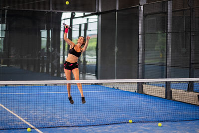 Woman playing padel in a blue grass padel court indoor - young sporty woman padel player 