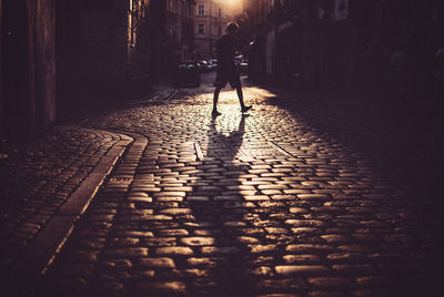 Silhouette man walking on street in city during sunset