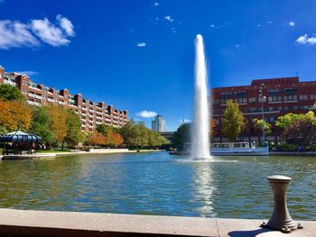 Fountain in front of buildings in town against blue sky