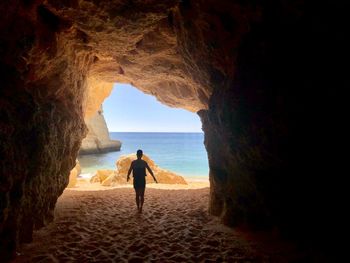 Rear view of man walking on sand in cave at beach