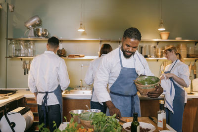 Male chef holding bowl while preparing food in commercial kitchen