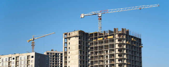 Low angle view of crane by building against clear sky