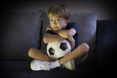 Portrait of boy with soccer ball sitting on sofa at home