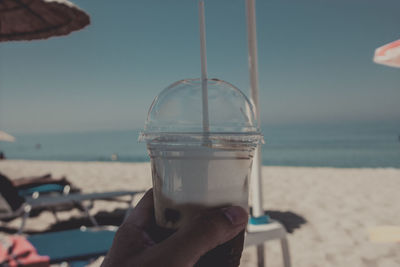 Close-up of hand holding drink at beach against sky