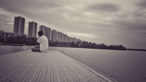 Rear view of man sitting on lake against sky