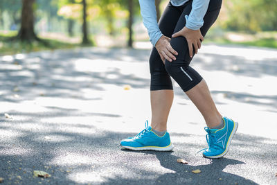 Low section of woman touching thigh in pain on road