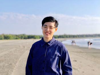 Young man standing at beach against sky