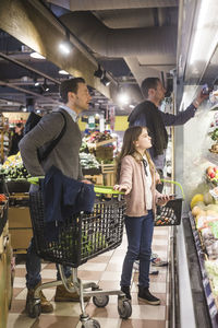 Father and daughter looking for fresh vegetables on shelves in grocery store