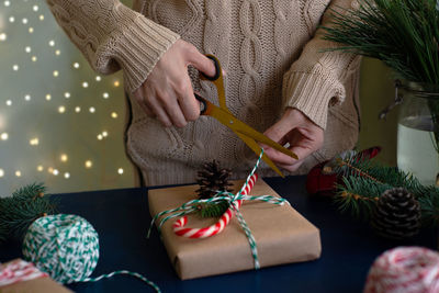 Woman wraps a handmade eco style christmas present in kraft paper and natural spruce branches