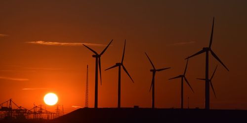 Silhouette windmills against orange sky