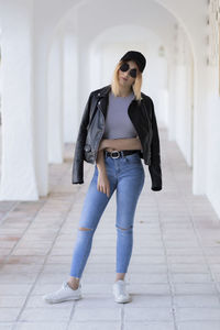 Portrait of young woman wearing sunglasses and leather jacket standing in corridor