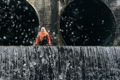 Woman crouching on waterfall