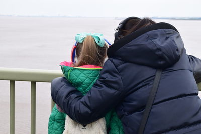 Rear view of woman with daughter standing against sky