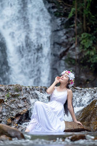 A beautiful young lady relaxes in nature near a waterfall.