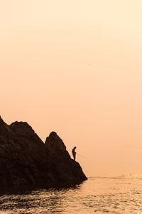 Silhouette rocks by sea against clear sky during sunset