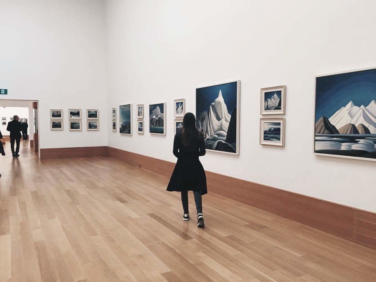 REAR VIEW OF WOMAN STANDING AGAINST WALL IN MUSEUM