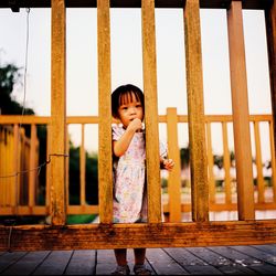 Portrait of girl standing on boardwalk seen through wooden railing