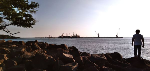 Rear view of men standing on rock by sea against clear sky