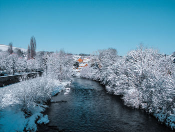 River amidst snow covered trees against clear blue sky