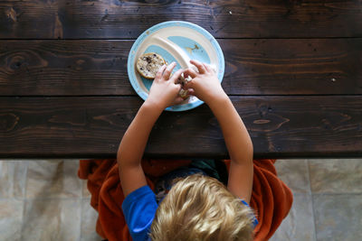 High angle view of boy eating bread while sitting on table at home