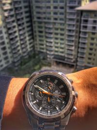 Close-up of hand holding clock against buildings