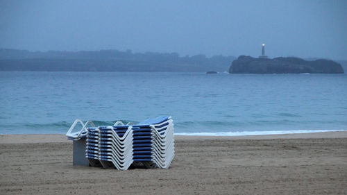 Deck chairs on beach against sky