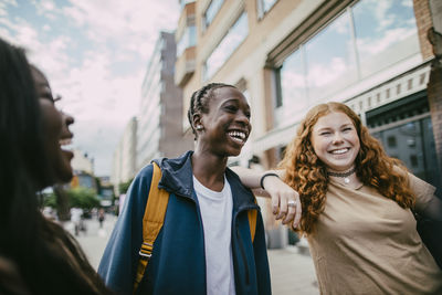 Happy teenage girl standing with hand on shoulder of male friend in city