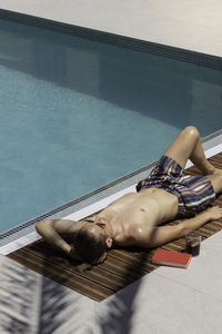 Vertical view of young man relaxed while sunbathing with a book and a palmtree leaf shadow