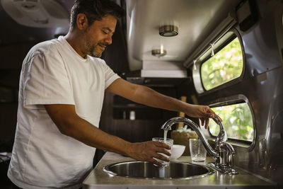 Smiling man filling drinking water through faucet in camper trailer