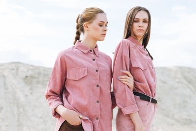 Fashion beauty portrait of young women sisters in pink organic velvet shirts on desert background