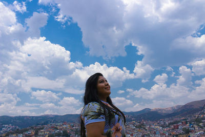 Side view of woman looking away while standing cloudy sky