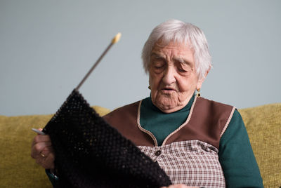 Senior woman knitting textile on sofa at home