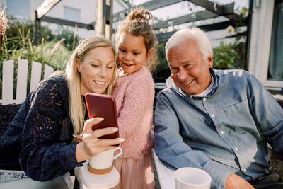 Smiling grandparent and granddaughter taking selfie with mobile phone while sitting in backyard