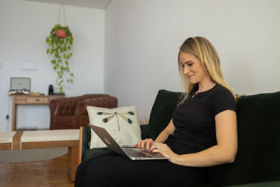 Woman working at home from couch with laptop on her lap. home office concept. gray notebook