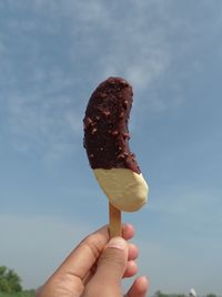 Cropped hand holding ice cream cone against sky