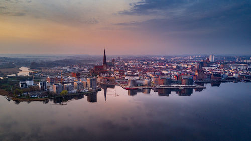 Cityscape by river against sky during sunset