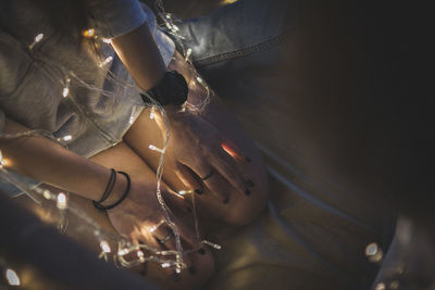 Midsection of woman with illuminated string lights kneeling on floor at home