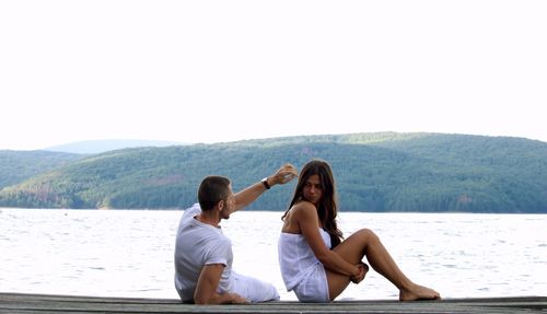 Young couple sitting on pier against lake