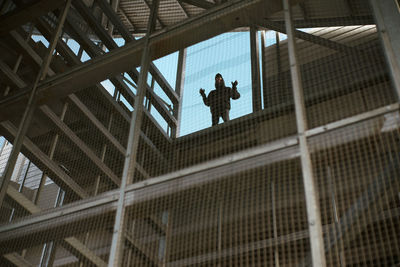 Low angle view of man standing by window seen through fence